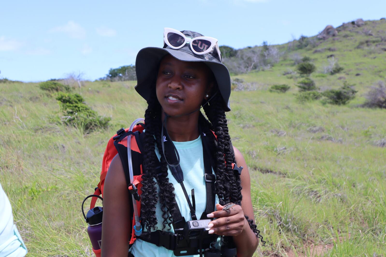 A young woman hiking through a field with a lizard in her hand