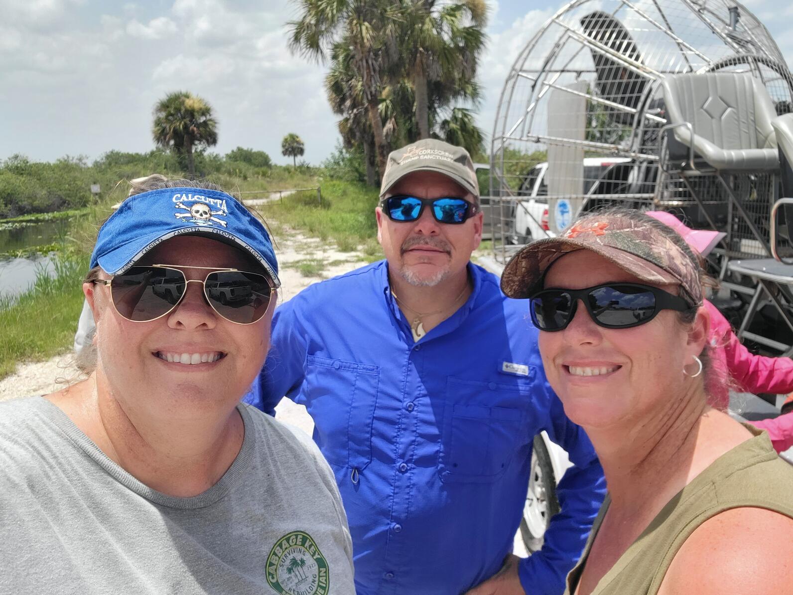 Three people standing in front of an air boat smiling for the camera