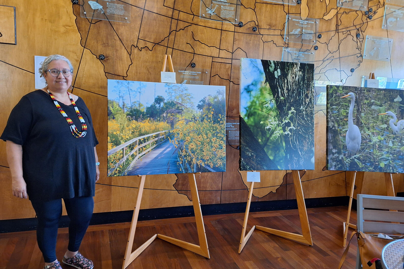 A woman standing next to 3 easels with nature photographs