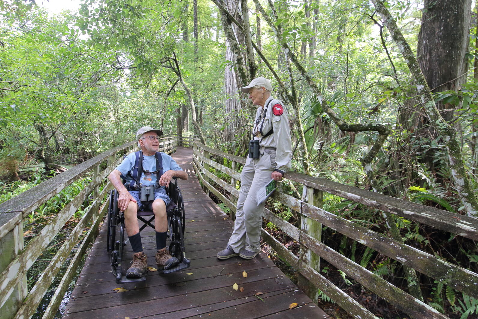 A man in a wheelchair speaking with someone in uniform on a boardwalk