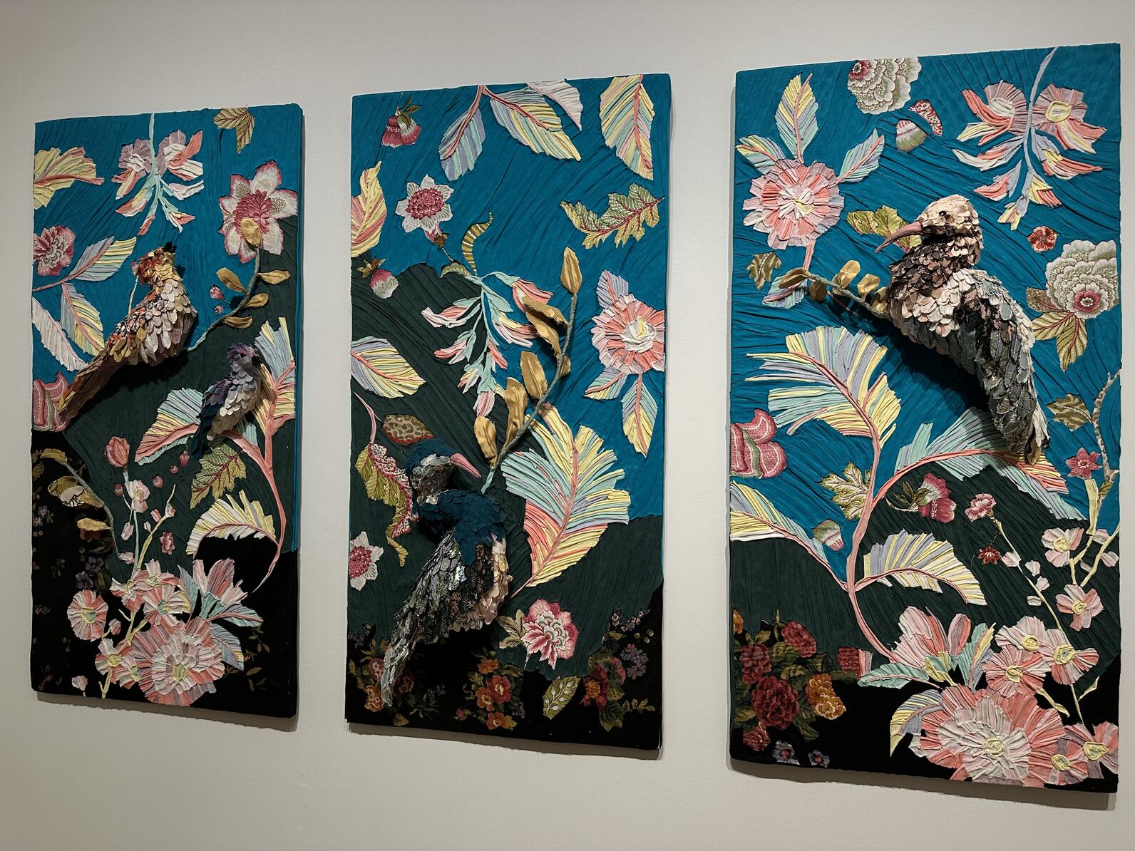 A three-panel art piece featuring birds, flowers, and leaves hung on a wall.