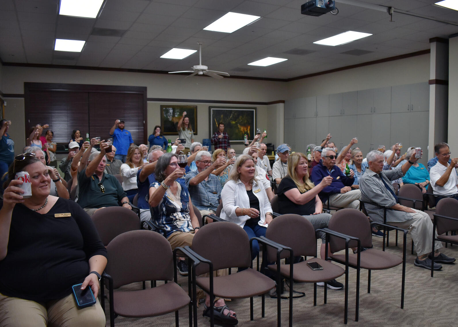 Photo of a room full of people seated with glasses raised.